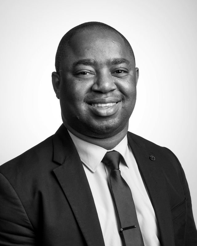 Frank Tsuro in a suit and tie, turned slightly to the right. Studio headshot in black and white.
